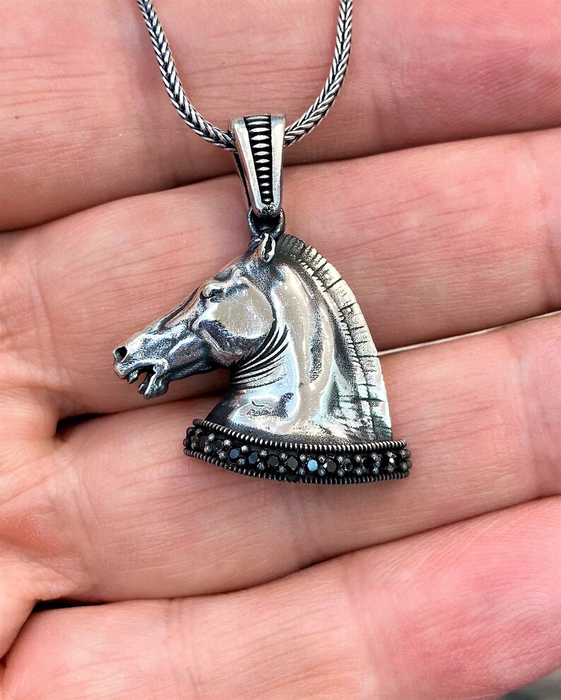 May include: Silver horse head pendant necklace with black gemstone accents. The pendant is detailed with a textured finish and a chain link necklace.