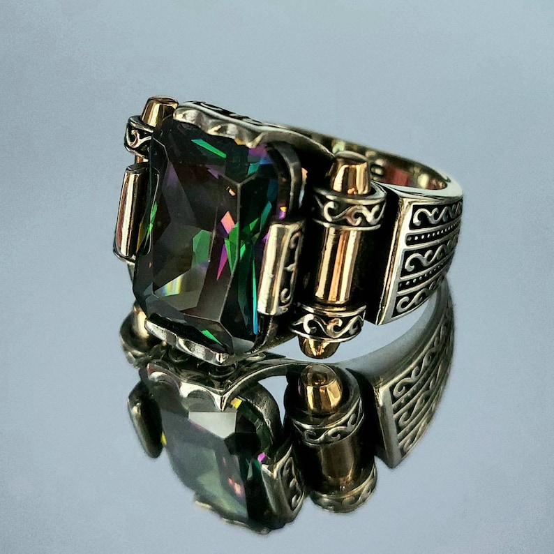 May include: A silver ring with a large, faceted, iridescent green gemstone set in a decorative, ornate setting. The ring has gold accents and a detailed design.