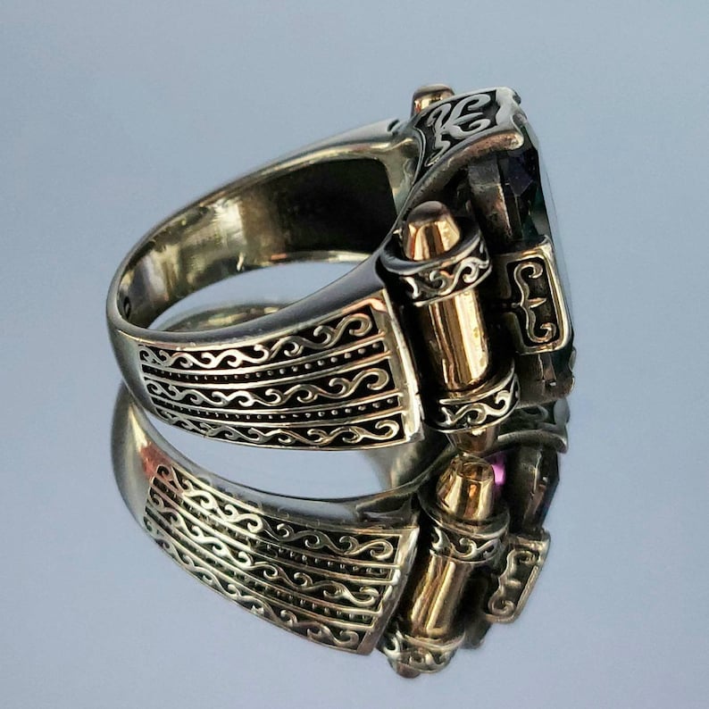 May include: A silver ring with a large, faceted, dark green gemstone. The ring has a decorative, ornate design with gold accents and a hinged band.