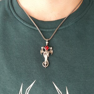 May include: A silver necklace with a pendant featuring a dragon wrapped around a sword with a red gemstone.