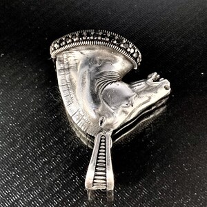 May include: A silver horse head pendant with black gemstone accents. The pendant has a detailed design and a textured surface.