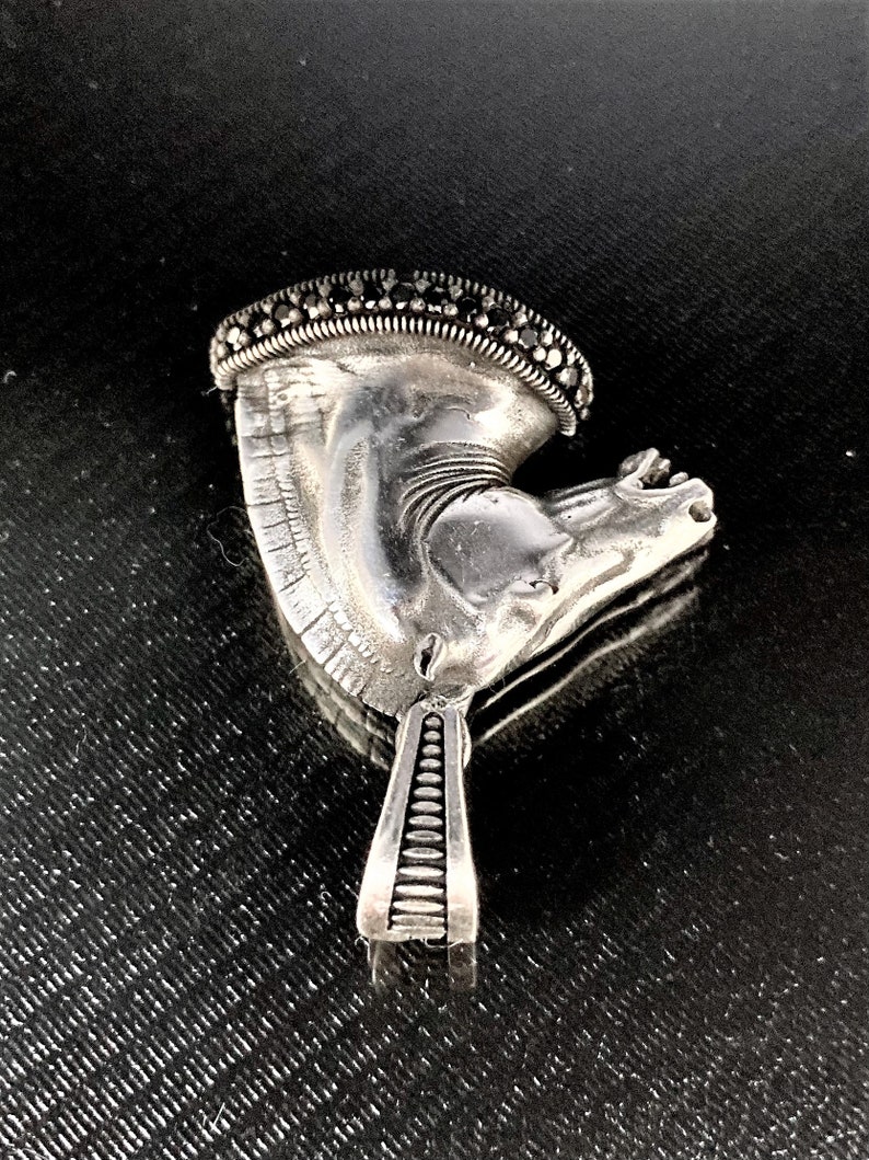 May include: A silver horse head pendant with black gemstone accents. The pendant has a detailed design and a textured surface.