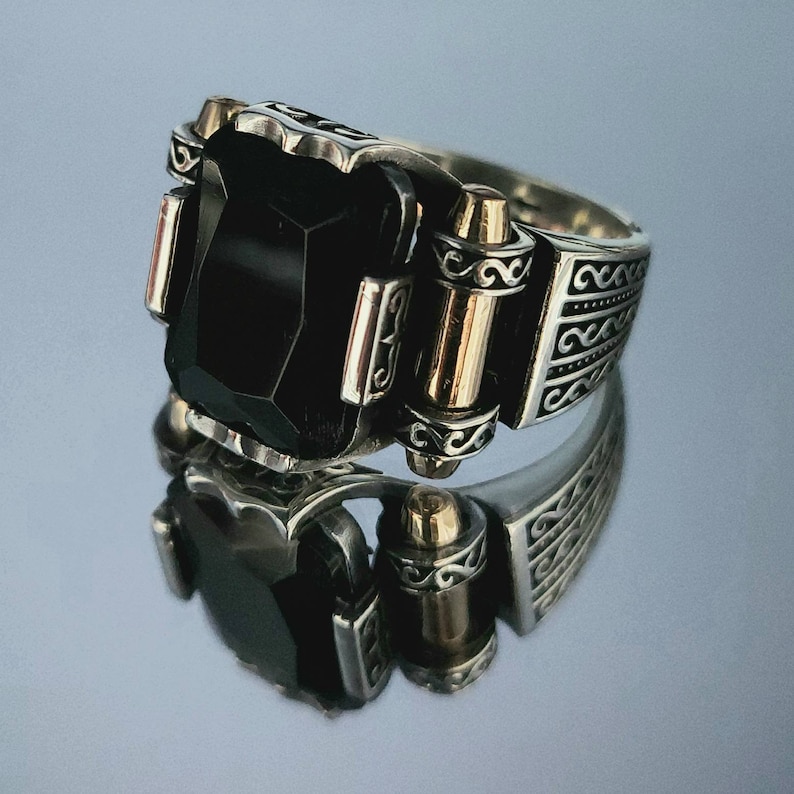 May include: A silver ring with a black gemstone and intricate details. The ring has a gold band and a decorative design.