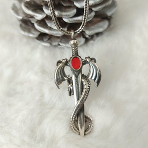 May include: A silver pendant necklace featuring a dragon wrapped around a sword with a red gemstone. The pendant has the inscription "925" on the sword.