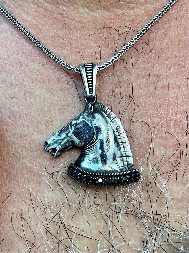 May include: A silver horse head pendant necklace with black gemstones around the base. The necklace is on a silver chain.
