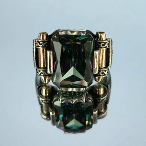 May include: A silver ring with a large, faceted, iridescent green gemstone set in a detailed, ornate setting. The ring has two gold accents on either side of the stone.