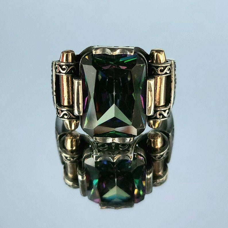 May include: A silver ring with a large, faceted, iridescent green gemstone set in a detailed, ornate setting. The ring has two gold accents on either side of the stone.