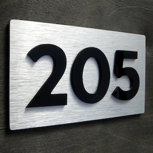 May include: A silver metal house number sign with black raised numbers reading "205".