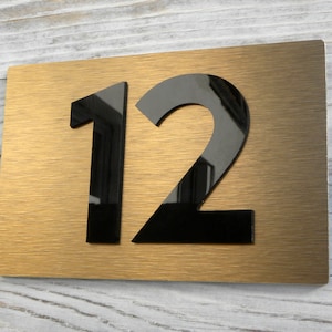 Może przedstawiać: Złoty metalowy znak z numerem domu z numerem 12 w czarnych, wypukłych literach.