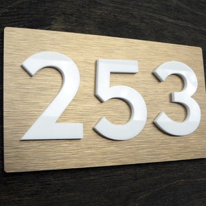 May include: White plastic house number plaque with the number 253 on a gold background.
