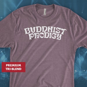May include: A mauve t-shirt with the text "BUDDHIST PRODIGY" in white, stylized lettering. The shirt is a premium tri-blend.