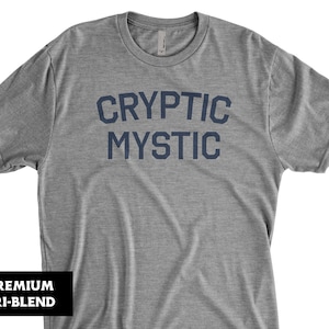 May include: A heather grey t-shirt with the text "CRYPTIC MYSTIC" printed in navy blue.