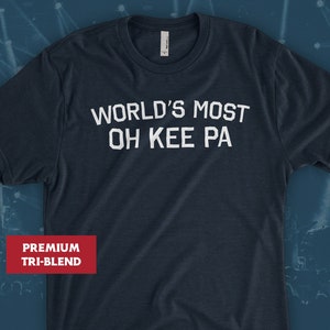 May include: A dark blue t-shirt with the text "WORLD'S MOST OH KEE PA" printed in white. The shirt is made of a premium tri-blend fabric.