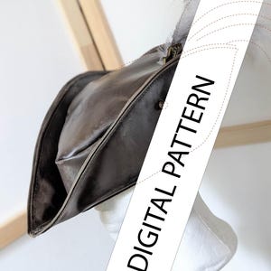 Può includere: Cappello tricorno in pelle marrone con dettaglio in piuma, esposto su una testa di manichino bianca. Il cappello ha un design da pirata classico con tesa rialzata. Il testo "DIGITAL PATTERN" è visibile.