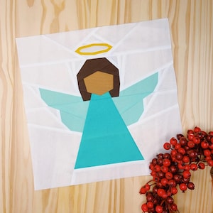 Puede incluir: Un ángel de tela blanca con un vestido turquesa, cabello marrón y un halo amarillo. El ángel está sobre un fondo de madera.