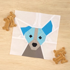 Op de afbeelding: Een papier-gepatchte hondenblok met een witte achtergrond, blauwe oren, grijs gezicht en zwarte ogen en neus.