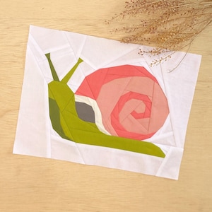 Puede incluir: Un bloque de colcha de papel con forma de caracol con un cuerpo verde y una concha rosa y blanca.