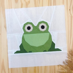 May include: A green frog with black eyes is made from fabric pieces and sewn together. The frog is on a white background.