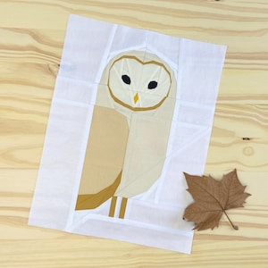 May include: A white fabric pattern with a brown and white barn owl design. The owl is made up of different fabric pieces sewn together.