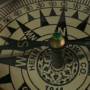 Puede incluir: Una brújula vintage con un diseño en blanco y negro. La cara de la brújula tiene una joya verde en el centro y las palabras "NW", "SM", "MS", "HENRY", "N", "OW & CO", "S" y "1941" están impresas alrededor del borde.