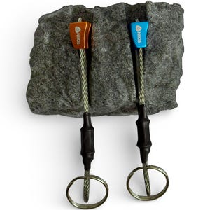 May include: Two climbing nuts with metal heads in orange and blue, each featuring the brand name NIKIS printed in white. The heads are attached to flexible steel cables with black heat-shrink tubing and circular metal rings at the ends.