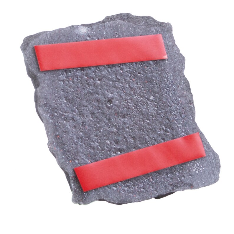 May include: A rectangular, dark grey stone-like plaque with a rough, textured surface. Two horizontal strips of red adhesive backing are attached to the front, positioned near the top and bottom edges of the piece, ready for mounting purposes.