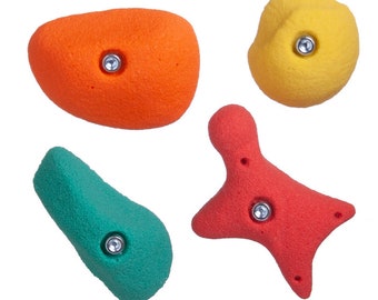May include: Four climbing holds in distinct shapes and colours: a large orange oval, a rounded yellow piece, a teal elongated form, and a red four-pointed star shape. Each hold features a central metal bolt hole for secure wall mounting.