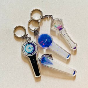 May include: Four different light-up keychain designs. The keychains are made of clear acrylic with a holographic finish. The designs include a blue and white star, a blue and white circle with a star, a blue and white diamond, and a blue and white circle with a star. The keychains are attached to silver key rings.