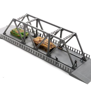 Op de afbeelding: Een grijs modelbrug met een metalen vakwerkconstructie. Twee speelgoedtanks, een groene en een bruine, staan op de brug. Miniatuursoldaten staan aan de rand van de brug en creëren een oorlogsscène.