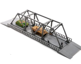 May include: A gray model bridge with a metal truss design. Two toy tanks, one green and one brown, are on the bridge. Miniature soldiers stand at the bridge's edge, creating a war scene.