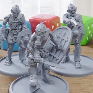 May include: Three gray miniature figures of warriors with weapons and shields, standing on gray circular bases. The figures are in a battle-ready stance, with a gas mask on one. Colorful dice are in the background.
