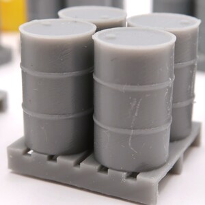 May include: Four gray plastic barrels stacked on a gray pallet. The barrels are all the same size and have a slightly textured surface.