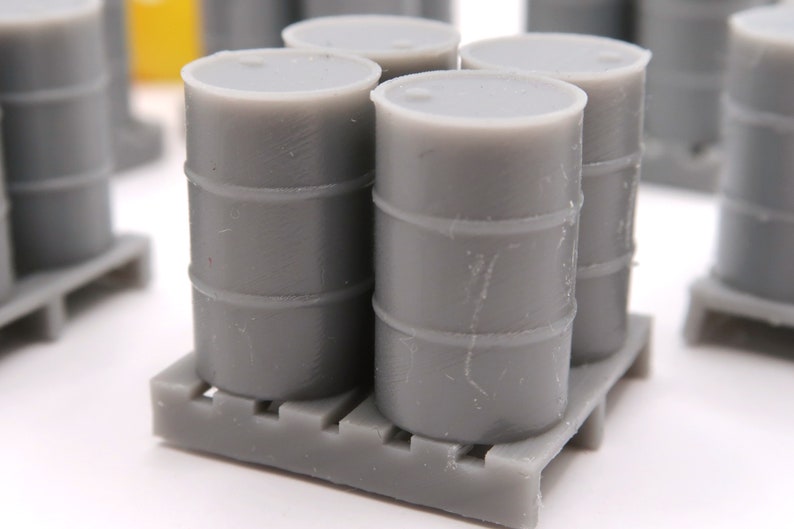 May include: Four gray plastic barrels stacked on a gray pallet. The barrels are all the same size and have a slightly textured surface.