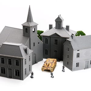 Op de afbeelding: Miniatuur grijze gebouwen, waaronder een kerk met toren en huizen, zijn gerangschikt rond een kleine tank. Groen gebladerte voegt kleur toe. Kleine beeldjes staan bij de tank en gebouwen.