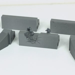 Puede incluir: Un conjunto de cinco secciones de pared de hormigón gris para una mesa de juego de guerra en miniatura. Las secciones incluyen una pared recta, una pared con una sección rota y tres piezas de esquina.