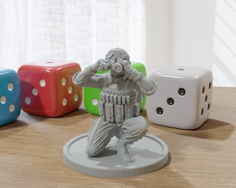 May include: A gray plastic miniature figurine of a soldier kneeling and looking through binoculars. The soldier is wearing a helmet, a vest with pouches, and pants. The figurine is on a round base.
