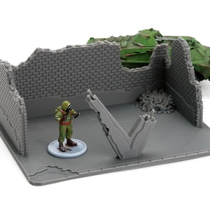 May include: Miniature gray brick building ruins with a green tank and a soldier figure. The soldier wears a green and brown uniform with a gas mask. The tank is green. The scene is set on a gray base.