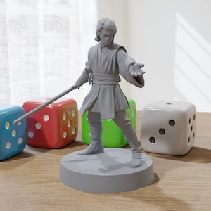 May include: A gray figurine of a character holding a lightsaber, standing on a gray circular base. Beside the figurine are four large dice in blue, red, green, and white. The dice have white dots. The background includes a window with white curtains.