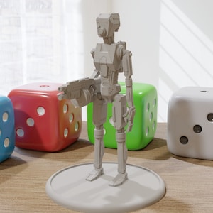 May include: A gray plastic miniature robot figure holding a gun, standing on a gray base. The robot is surrounded by four dice in different colors: blue, red, green, and white.