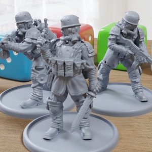 May include: Three gray miniature figurines of soldiers in combat gear, including helmets, gas masks, and weapons. Each figure stands on a circular base. Colorful dice are in the background.