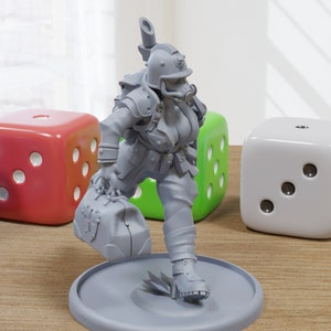 Puede incluir: Una miniatura gris impresa en 3D de una figura femenina que lleva un casco y lleva una bolsa médica. La figura está de pie sobre una base gris y está rodeada de dados.