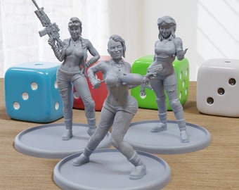May include: Three gray painted figurines of women with different hairstyles and clothing. The figures are standing on round bases. The figures are posed in action poses. The figures are on a wooden surface with two blue and white dice and one green and white dice.