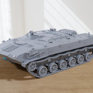 Puede incluir: Maqueta gris claro de un vehículo blindado de transporte de personal (APC) o tanque, con orugas, ruedas y una torreta detalladas. El modelo se encuentra sobre una superficie de madera, mostrando su intrincado diseño y temática de vehículo militar.