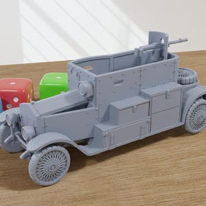 May include: A grey model of an armoured car with a machine gun mounted on top. The car has a boxy design with multiple compartments on the sides. The model is sitting on a wooden surface.