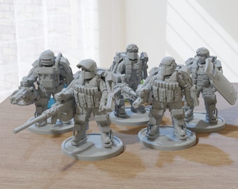 以下が含まれることがあります： 未来的な鎧を着た兵士の灰色のミニチュアフィギュアのグループ。それぞれが円形の台座に立っています。一部のフィギュアは、重機関銃や盾などの武器を持っています。フィギュアは木製の表面に配置されています。