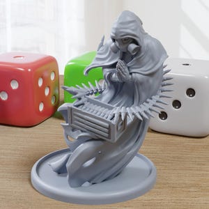 May include: A gray figurine of a hooded figure wearing a gas mask, with hands clasped in prayer. The figure is surrounded by large, colorful dice: blue, red, green, and white. The figurine sits on a round base.