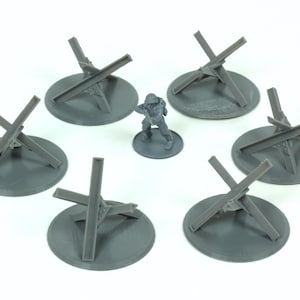 May include: A set of seven grey plastic toy anti-tank obstacles, also known as Czech hedgehogs, on grey circular bases. A grey plastic toy soldier stands in the centre.