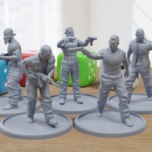 Peut inclure: Cinq figurines en plastique gris représentant des personnes vêtues de vêtements décontractés et tenant des armes. Les figurines sont posées sur des socles ronds gris. Les figurines sont disposées en demi-cercle sur une surface en bois.