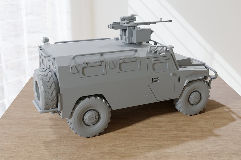 May include: A gray military armored vehicle with a mounted machine gun on top. The vehicle has a spare tire on the back and a roll cage.