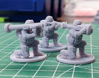 May include: Three gray plastic miniature figures of soldiers kneeling and holding a rocket launcher. The figures are on round bases.